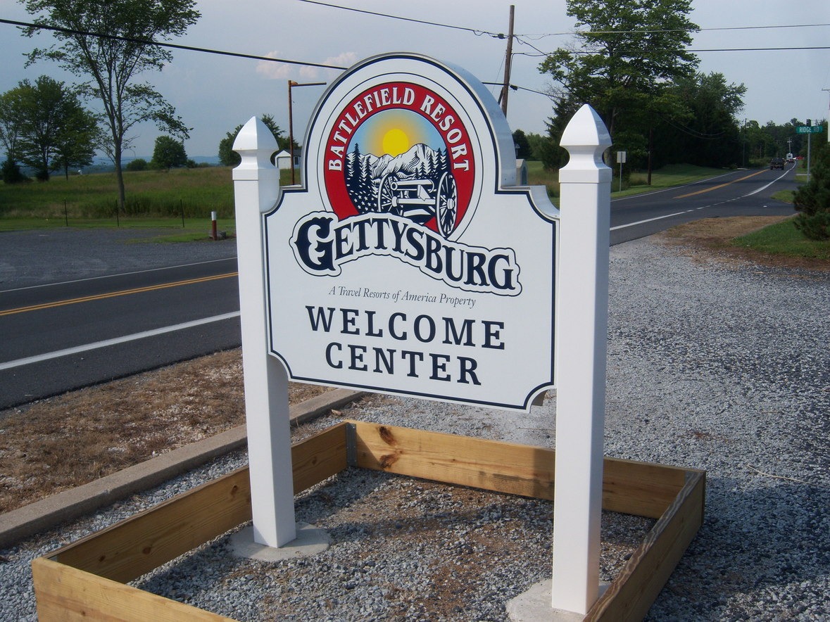 Gettysburg Battlefield Resort Welcome Center sign by a roadside, with trees and a clear sky in the background.