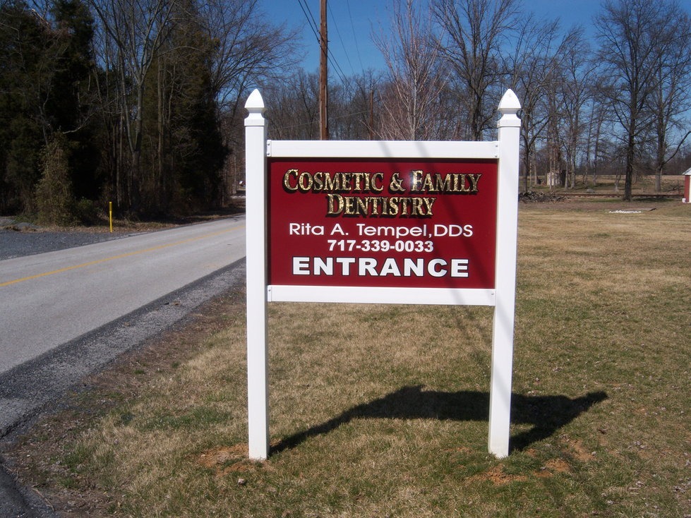 A red and white sign reads "Cosmetic & Family Dentistry, Rita A. Tempel, DDS, 717-339-0033, Entrance" by a roadside.