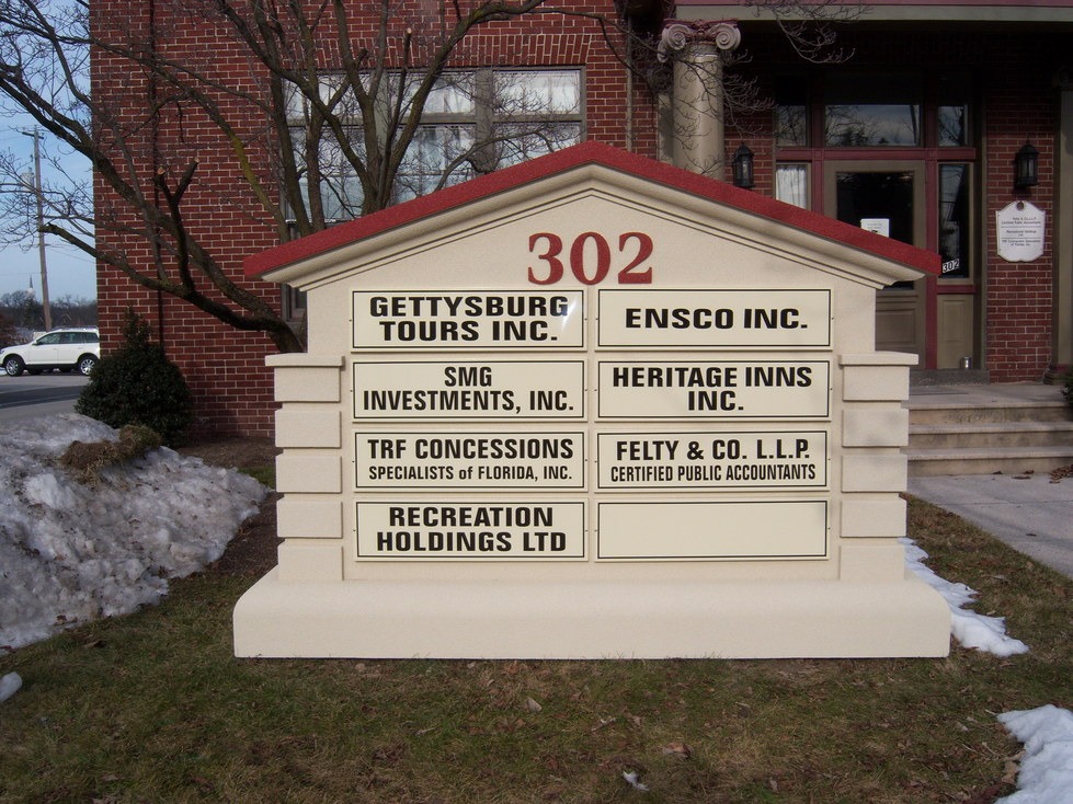 Outdoor directory sign for building 302 listing eight business names in front of a brick building and some snow on the ground.