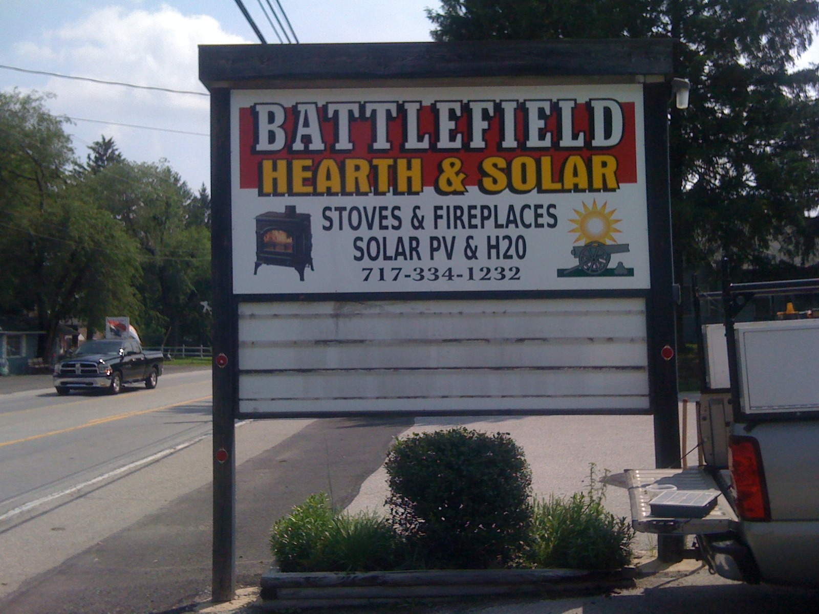 Outdoor sign for Battlefield Hearth & Solar advertising stoves, fireplaces, solar PV, and H2O with phone number.