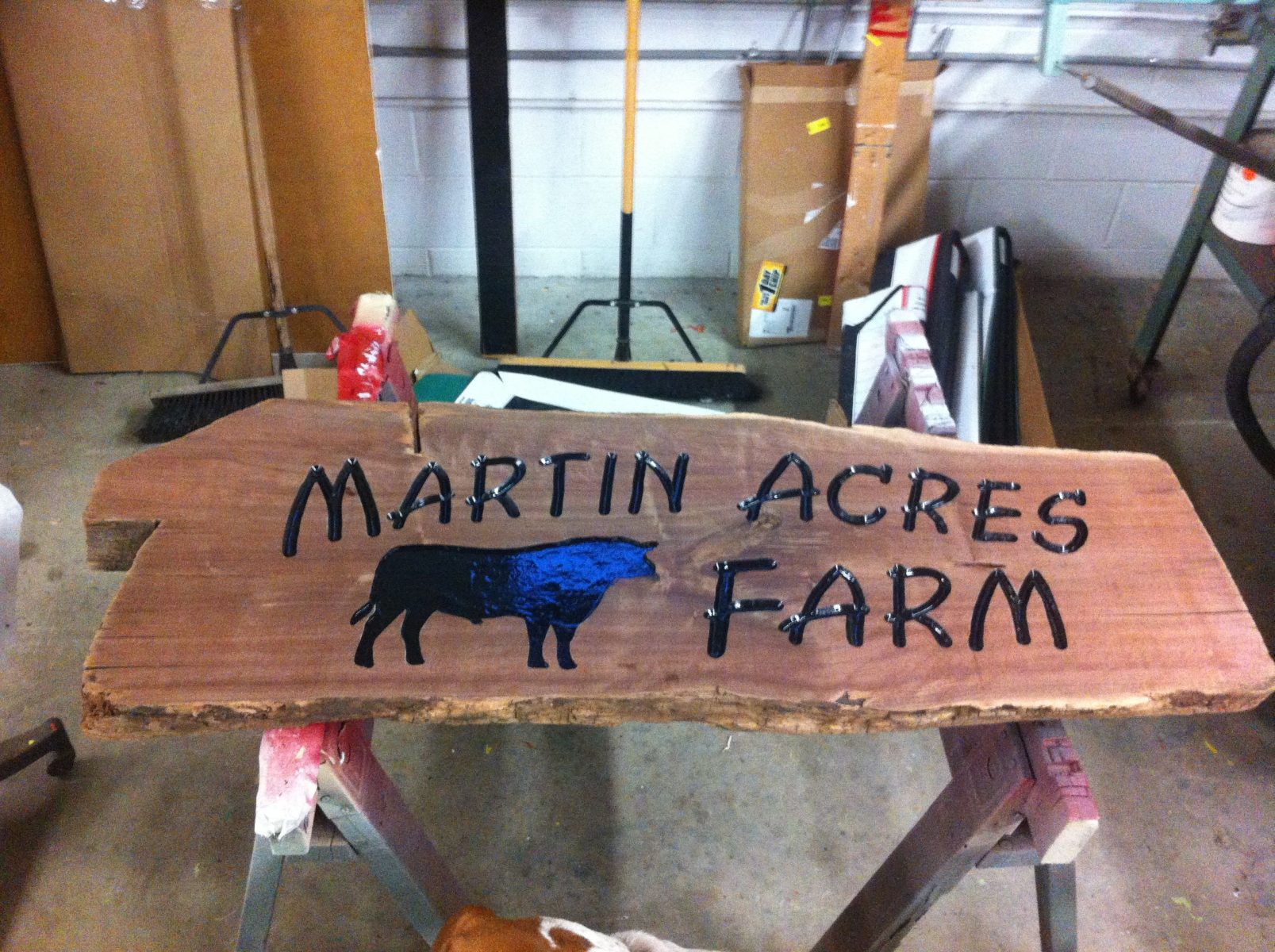 A wooden sign reads "Martin Acres Farm" with a silhouette of a bull, placed on a workbench in a workshop.