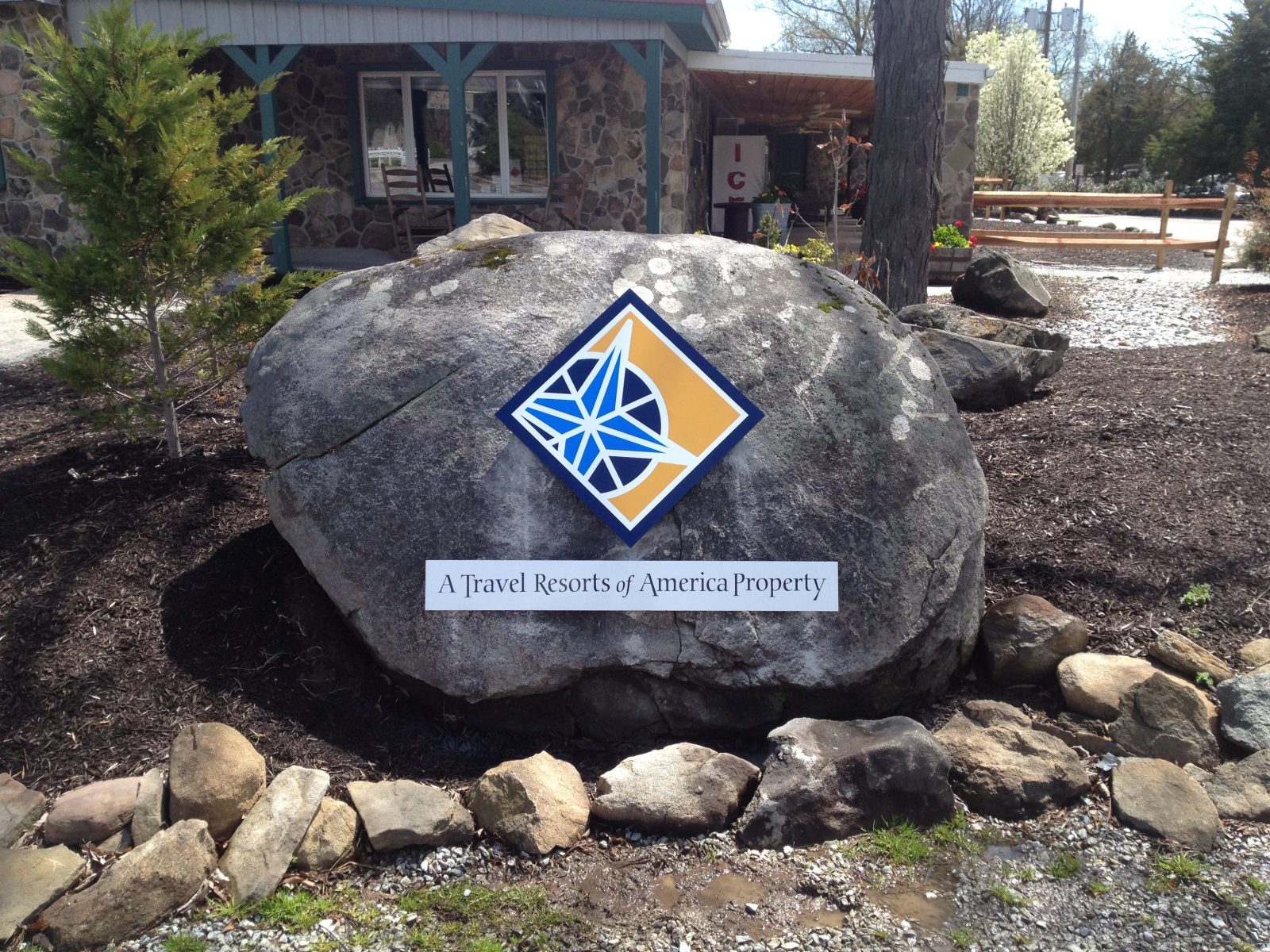 Large rock outside building displaying a blue and yellow logo and sign reading "A Travel Resorts of America Property.