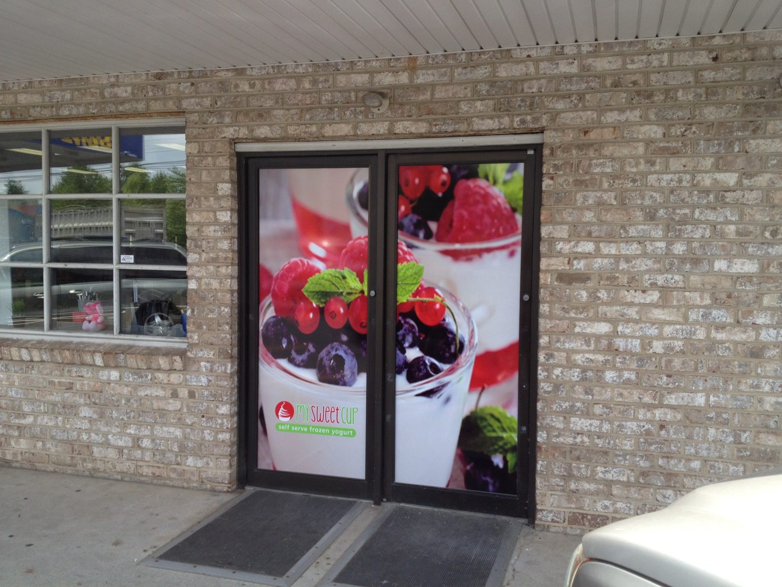 Glass door with a large image of berry parfaits and the Sweet Cup logo on a brick building exterior.