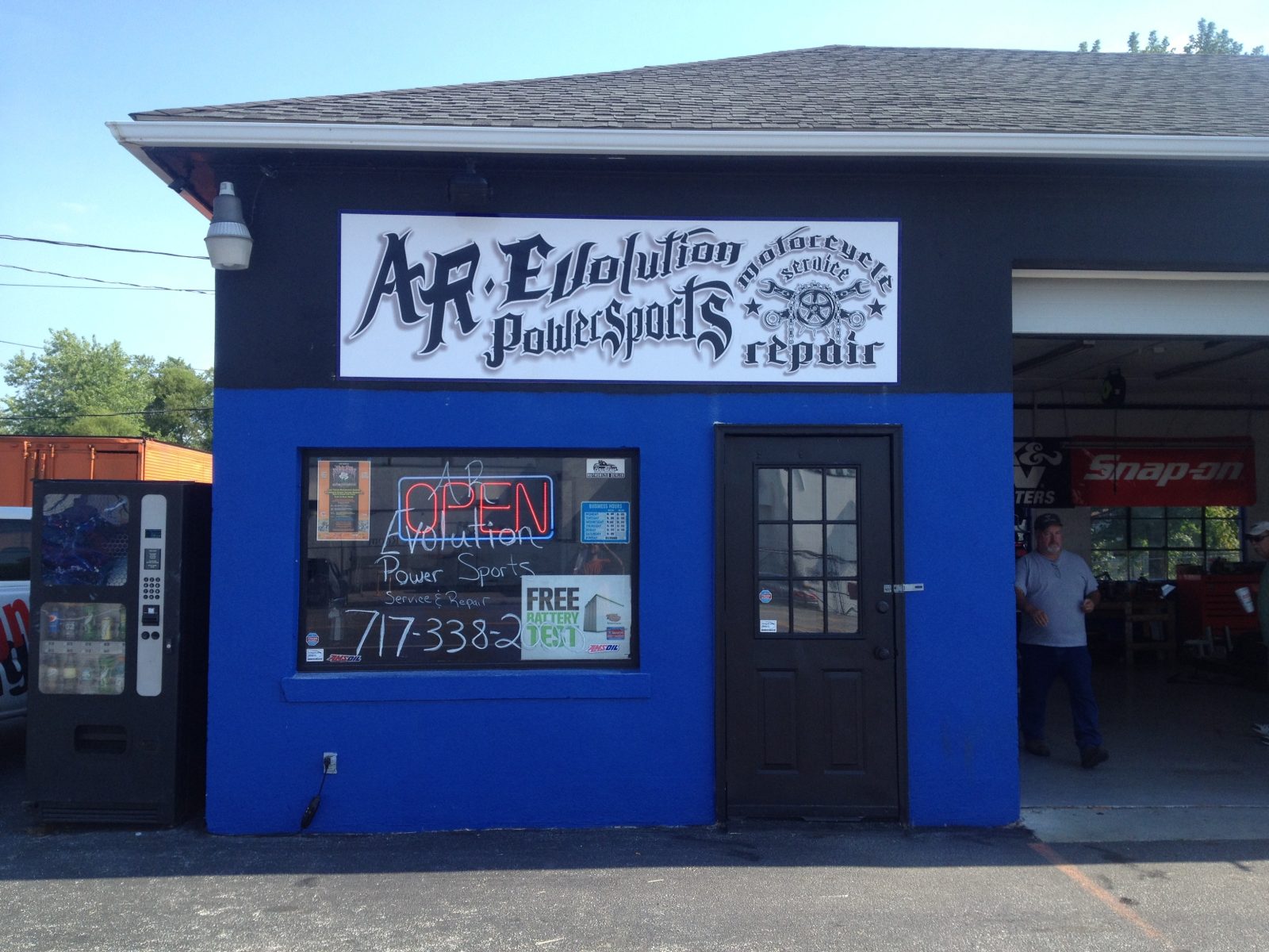 Blue motorcycle repair shop with "AR Evolution Powersports" sign, vending machine, and open garage door visible.