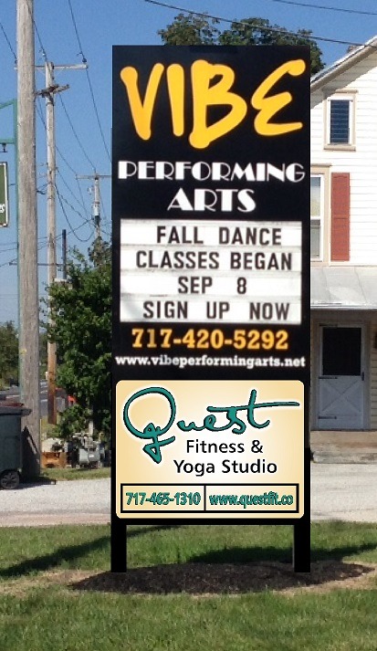 Outdoor sign for Vibe Performing Arts and Quest Fitness & Yoga Studio with info, phone numbers, and website URLs.