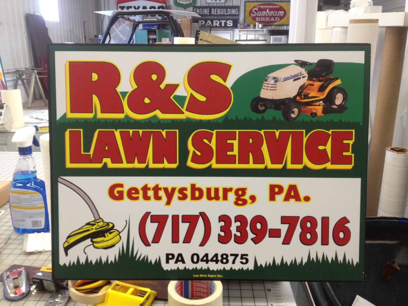 A sign for R&S Lawn Service in Gettysburg, PA, includes contact info, a lawnmower, and a trimmer illustration.