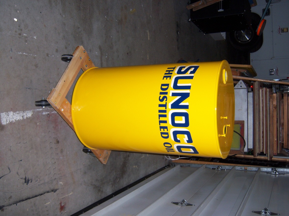 A large yellow barrel labeled "SUNOCO THE DISTILLED OIL" sits on a wooden dolly in a garage.