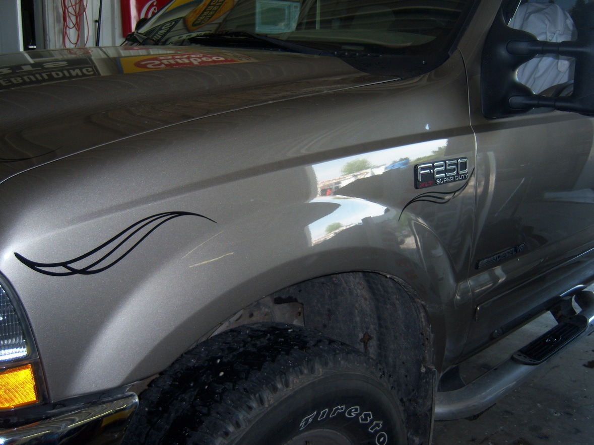 Close-up of the front side of a brown Ford F-250 truck with a black decal and Firestone tire visible.