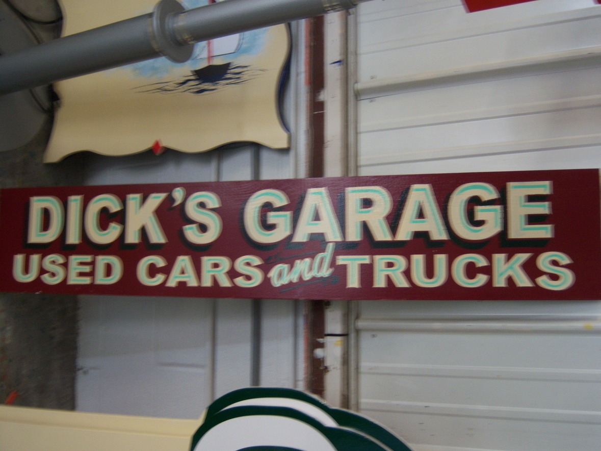 A red sign reads "Dick's Garage Used Cars and Trucks" in bold, multicolored letters on a wall.