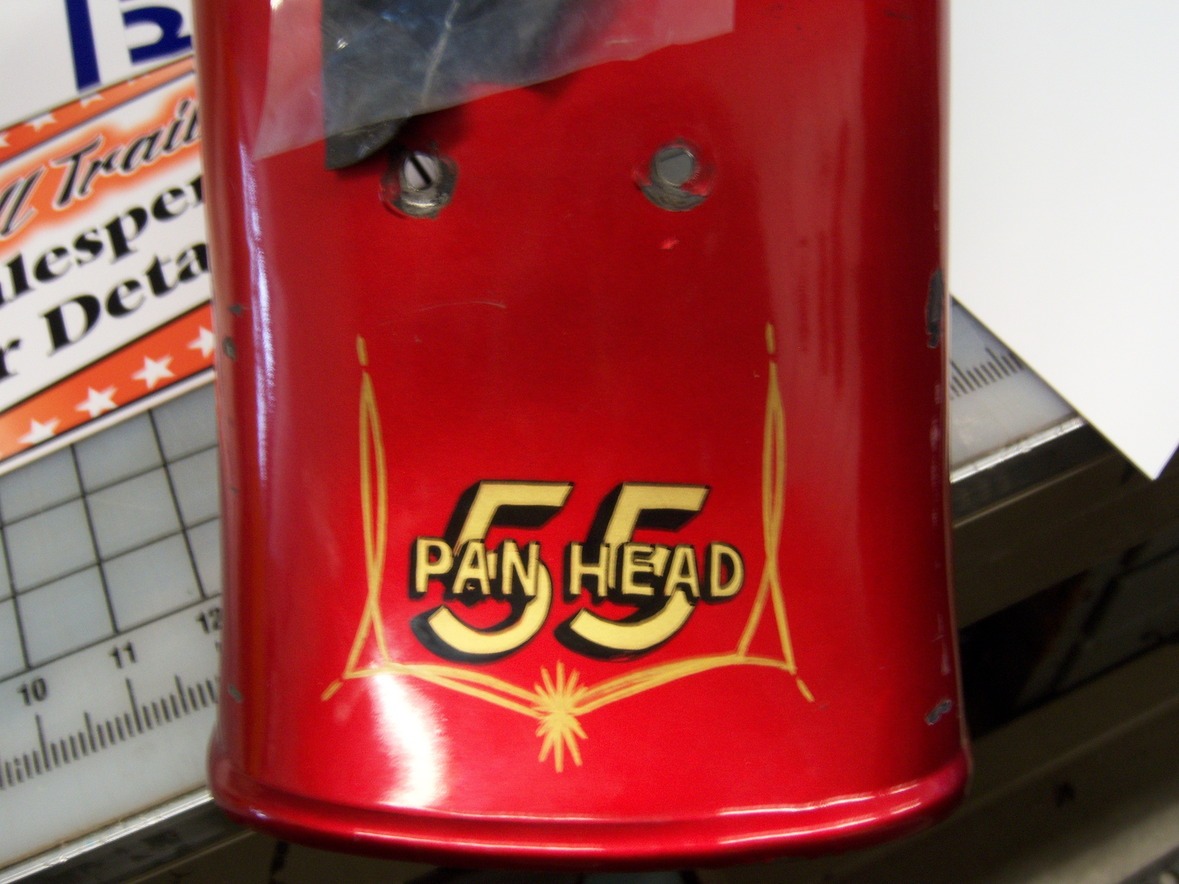 Red metal piece with "55 Pan Head" in yellow retro-style text and two holes near the top.