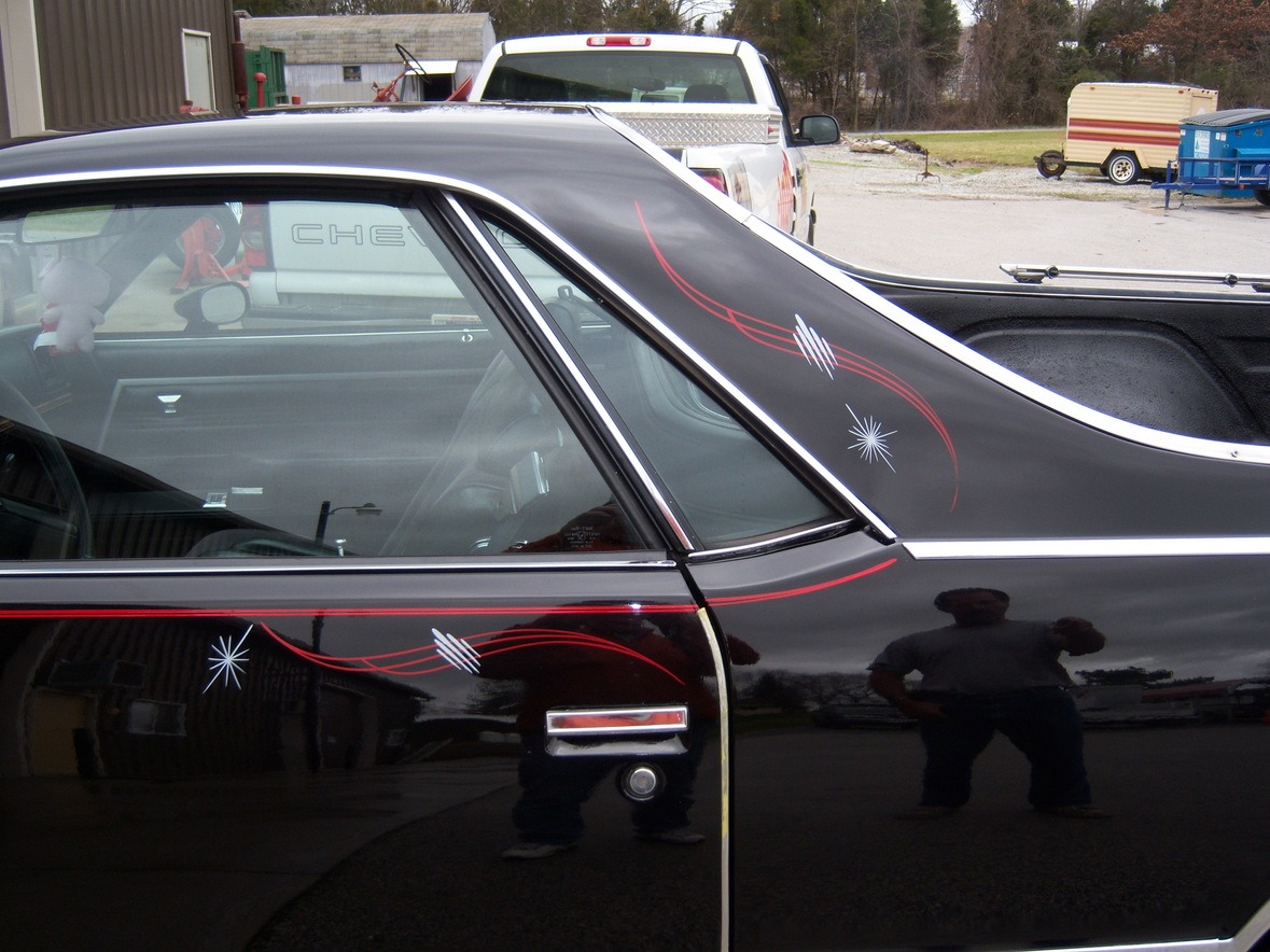 Close-up of a black car with red and white pinstriping, showing the rear side door and window, with reflections on the surface.