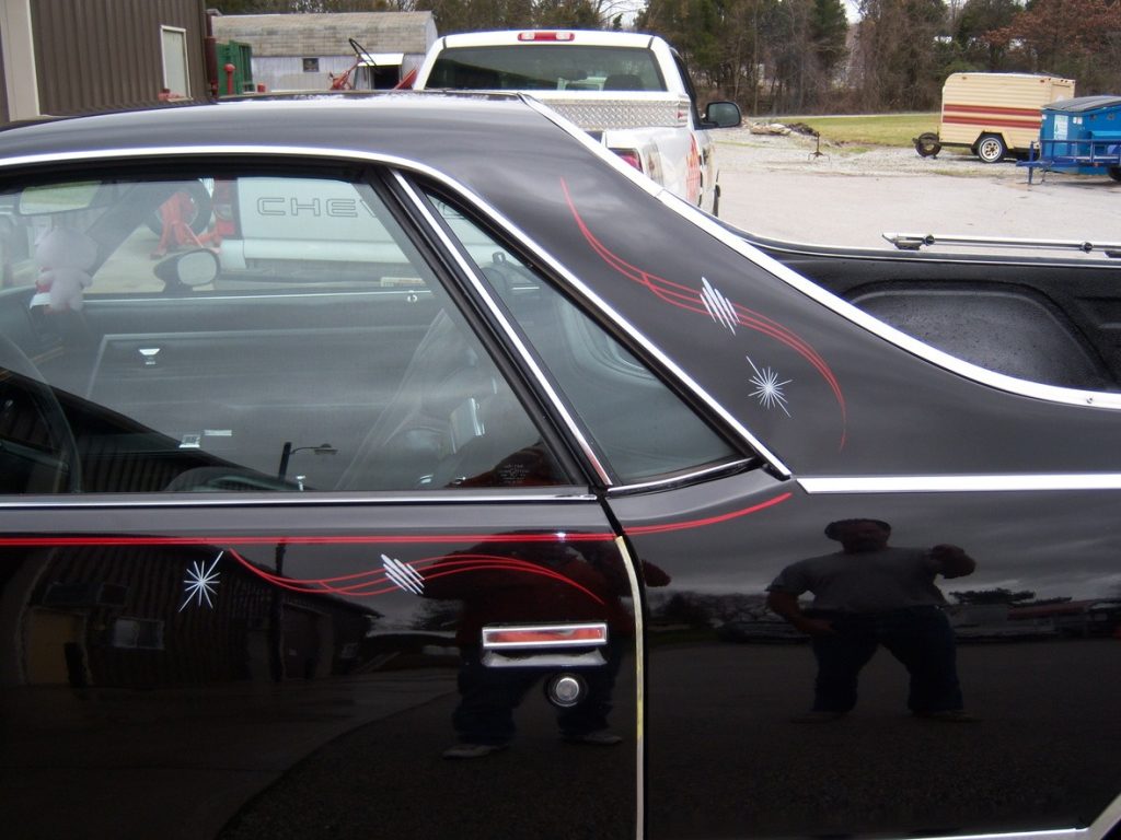 Black car with red and white pinstripe designs on the side, parked outdoors with reflections visible on the door.